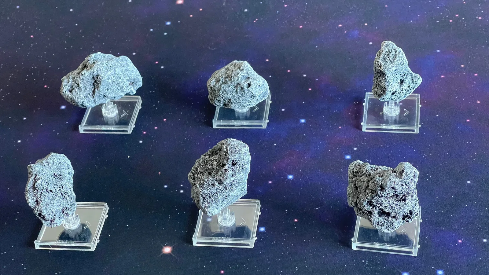 All six painted asteroid miniatures on their clear flight stands against a starfield.