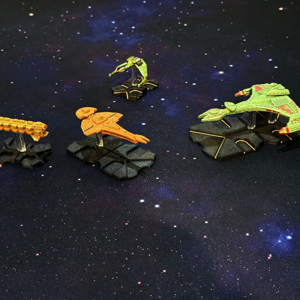 Black and color-inlaid 3D-printed ship bases on a starfield play surface, holding tokens for a Star Trek space combat game.