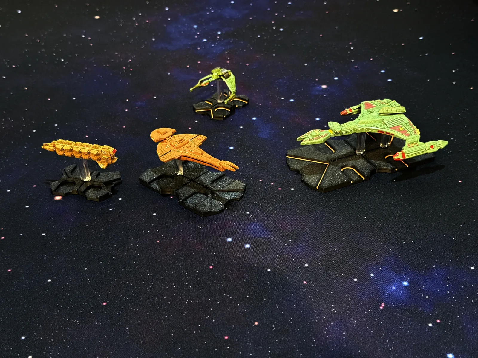 Black and color-inlaid 3D-printed ship bases on a starfield play surface, holding tokens for a Star Trek space combat game.