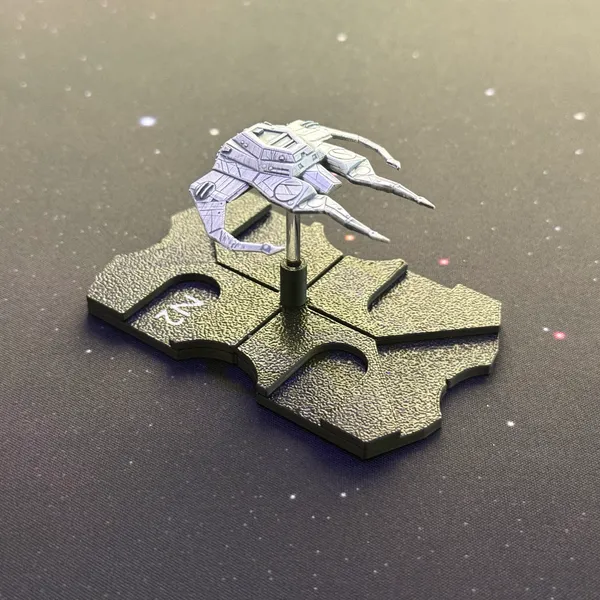 Painted 3D-printed miniature starship, a gray angular hull with long thin spindly legs, on a black printed base with clear peg, on a starfield play mat.