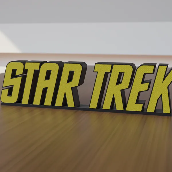 Freestanding 3D-printed logo sign, front view, yellow lettering on a black body, 300mm size, standing on a wooden table.